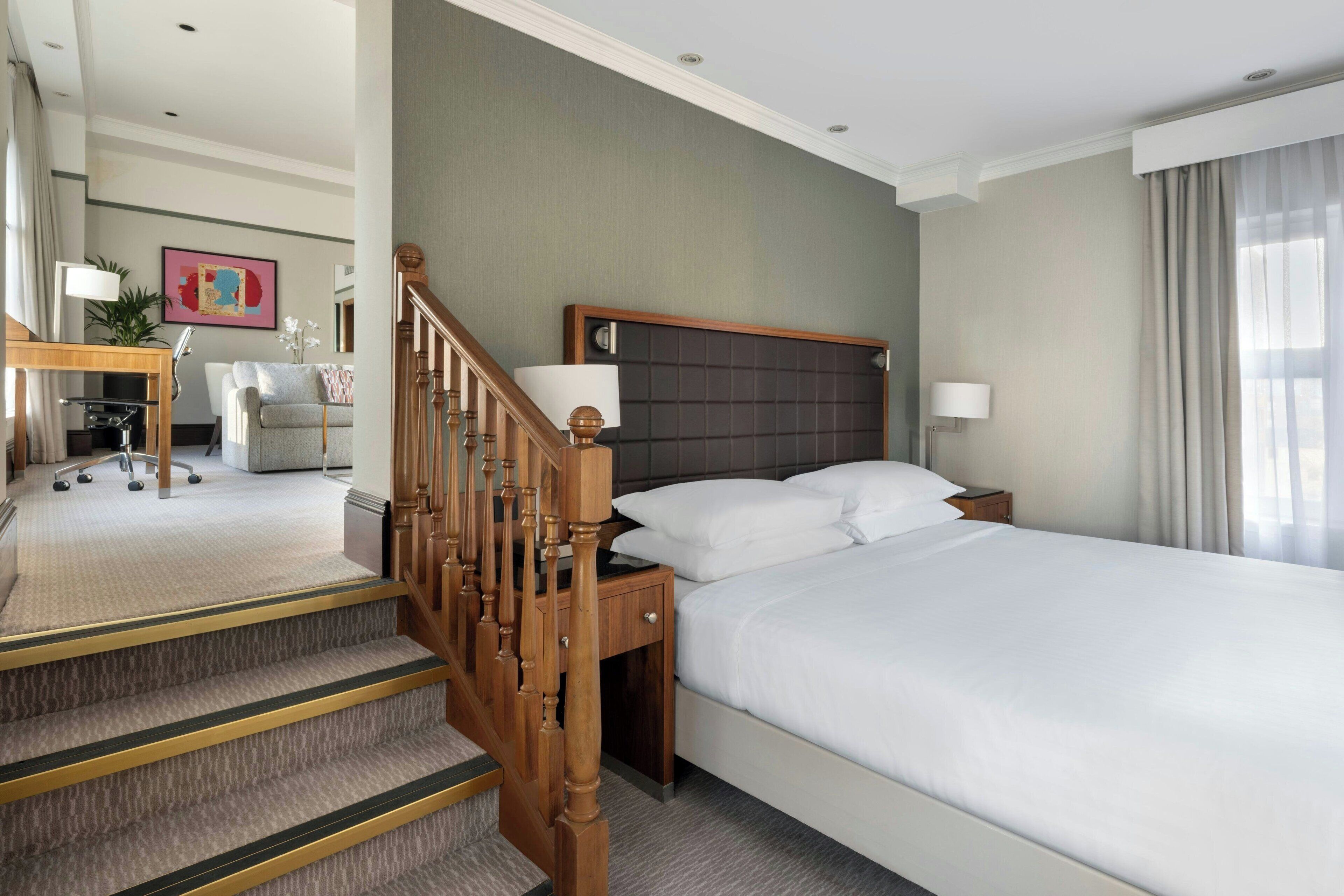 A hotel room with a bed, a desk, a chair, and a staircase.
