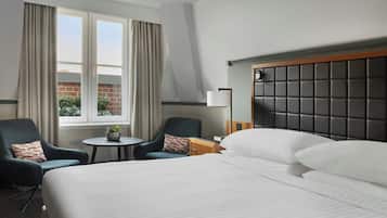 A hotel room with a large bed, two armchairs, a small round table, and a window with curtains.