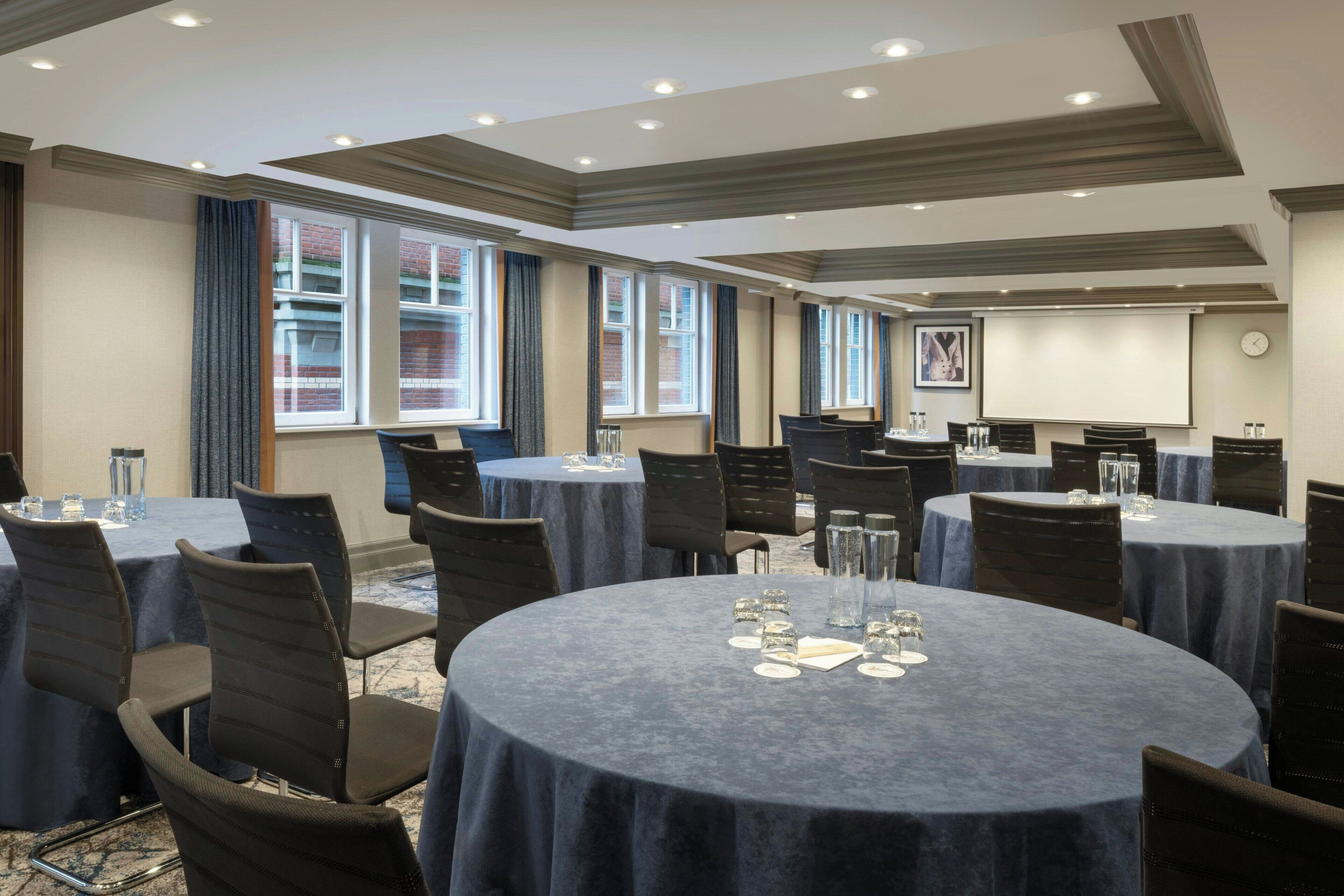 A conference room with multiple round tables, each with chairs and glassware.