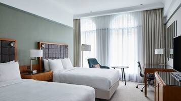 A hotel room with two beds, a desk, a chair, a television, and a large window with curtains.