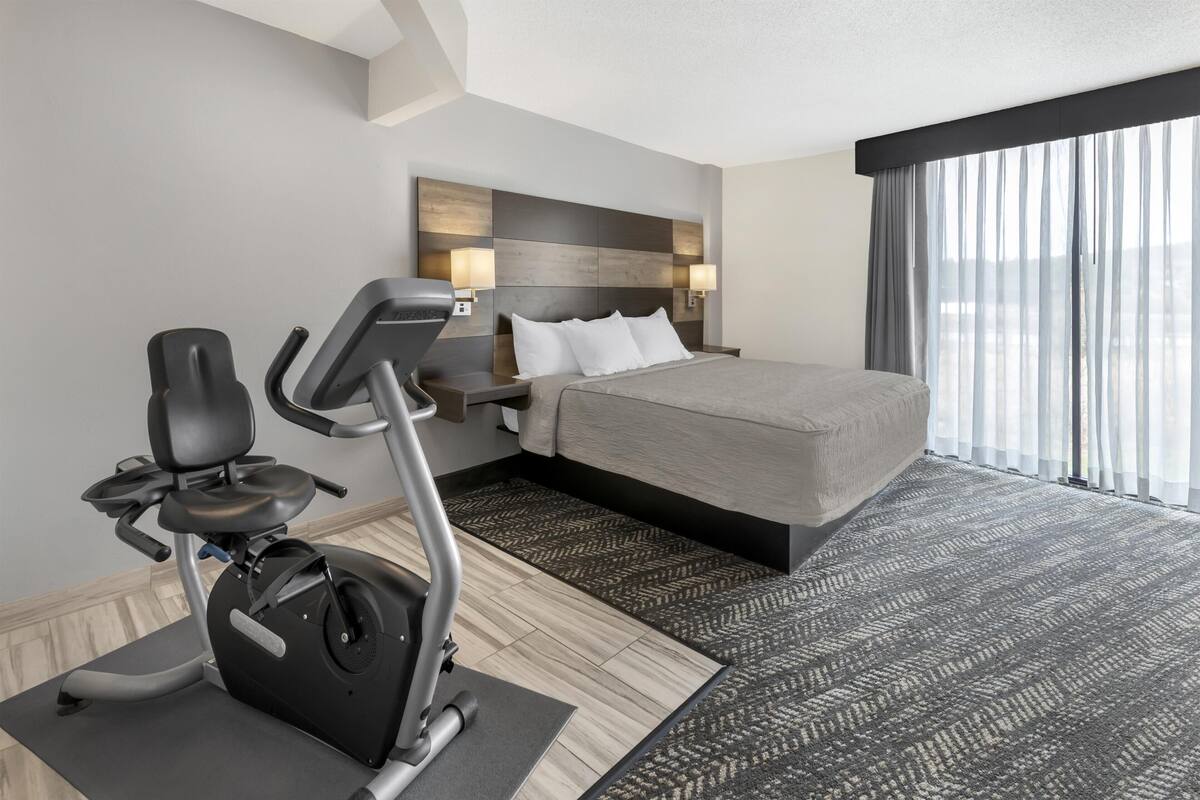 Ein Hotelzimmer mit Bett, Trainingsgeräten, einem großen Fenster mit Vorhängen und einem modernen Kopfteil.