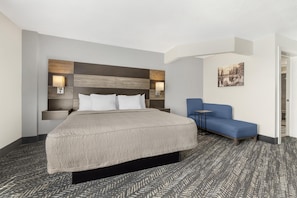 A hotel room with a bed, a blue armchair, a nightstand, and a wall-mounted lamp. - Best Western Plus Wausau Tower Inn (Wausau)