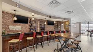Un espace bar avec un mur en briques, de nombreux tabourets de bar, une longue table en bois et un téléviseur fixé au mur.
