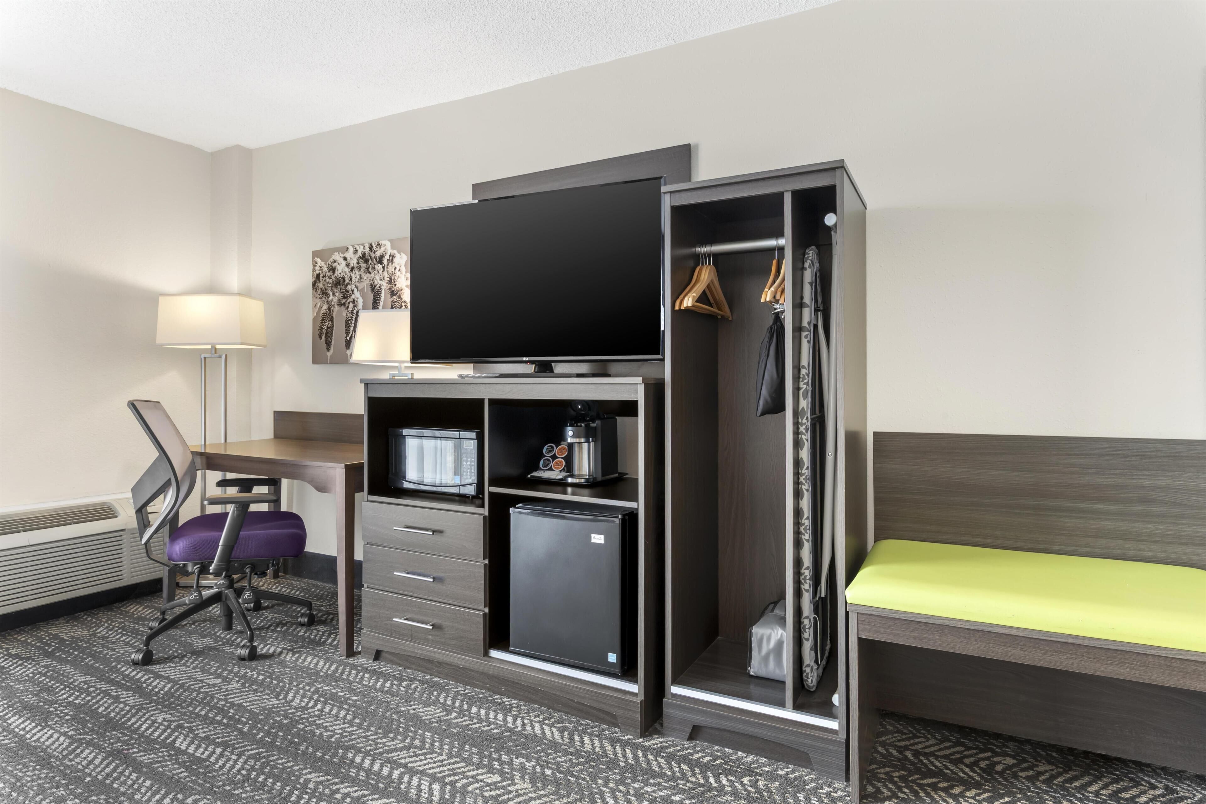 Una habitación de hotel con escritorio, silla, televisión, mini refrigerador y una cama.