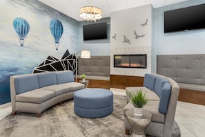 A modern living room with a sectional sofa, a round ottoman, a fireplace, and a wall-mounted TV. - Best Western Plus Wausau Tower Inn (Wausau)
