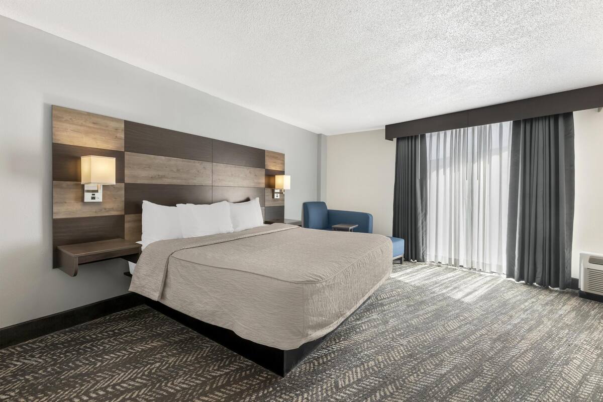 Ein Hotelzimmer mit einem Bett, Nachttischlampen, einem Schreibtisch, einem Stuhl und einem großen Fenster mit Vorhängen.