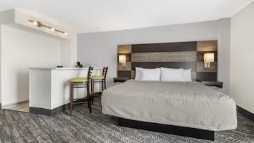 A hotel room with a bed, a desk, two chairs, and a patterned carpet.