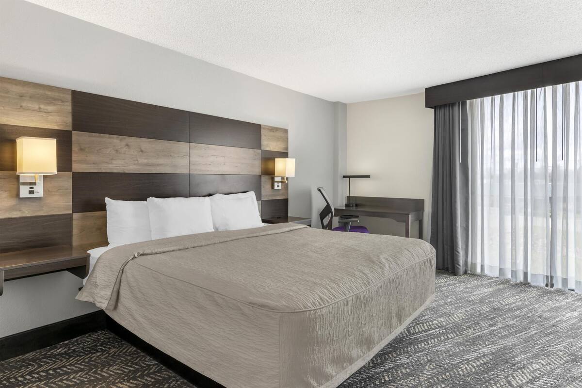 Ein Hotelzimmer mit einem großen Bett, Nachttischen, einem Schreibtisch und Blick ins Freie.