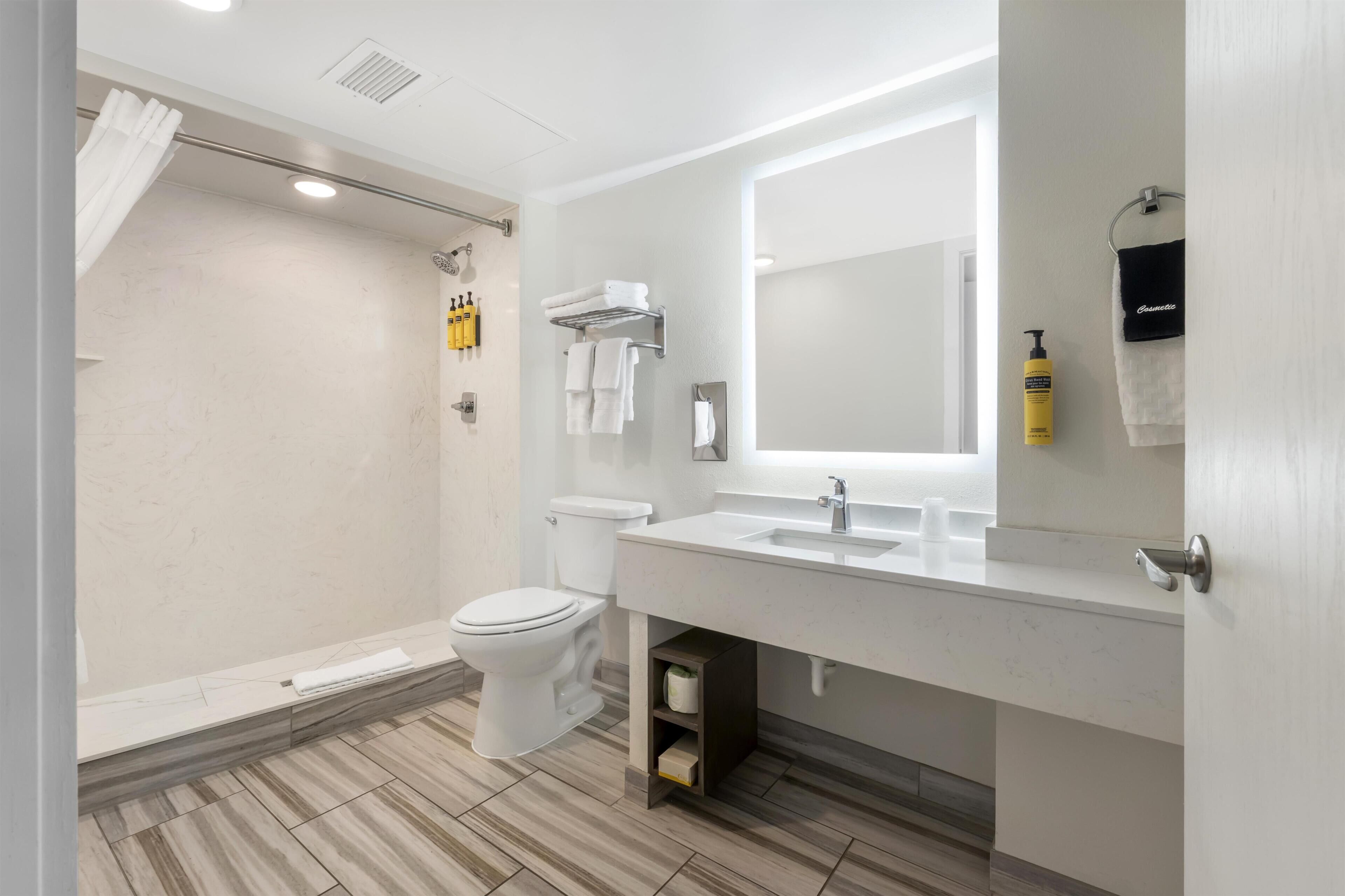 A modern bathroom with a shower, toilet, and sink, featuring a mirror, towel rack, and storage cabinet.