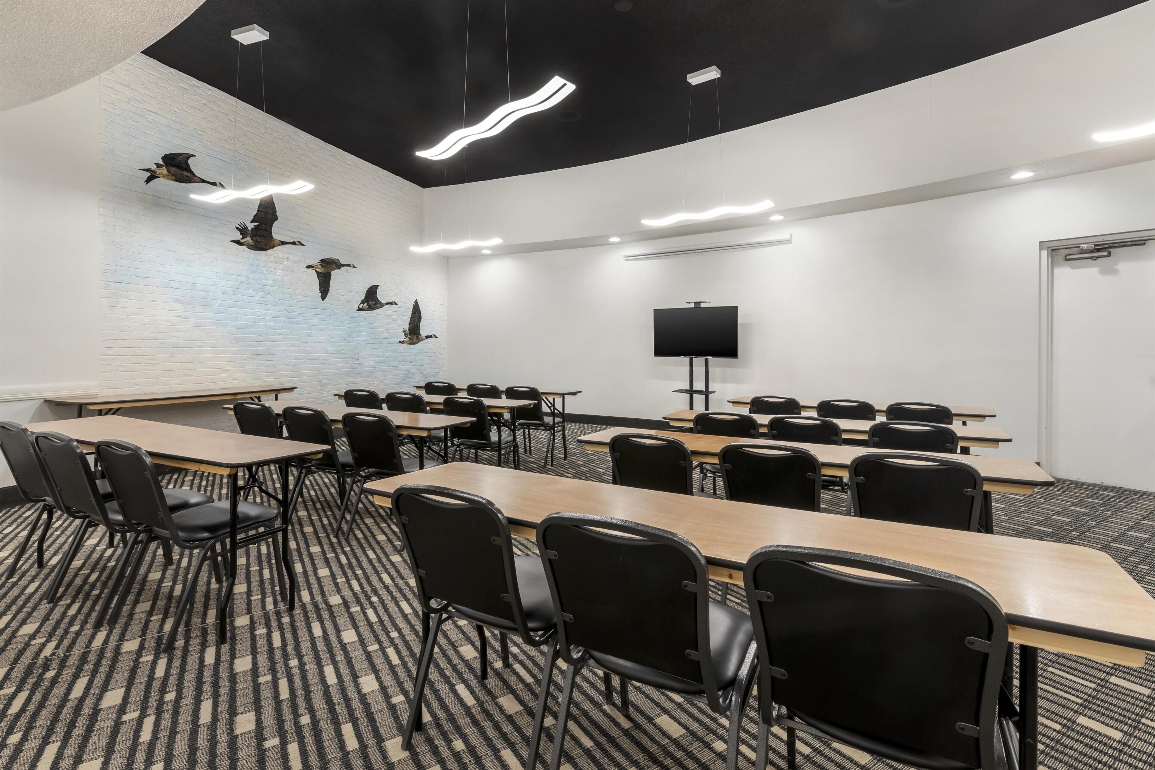 A conference room with tables, chairs, a projector screen, and a wall-mounted TV.