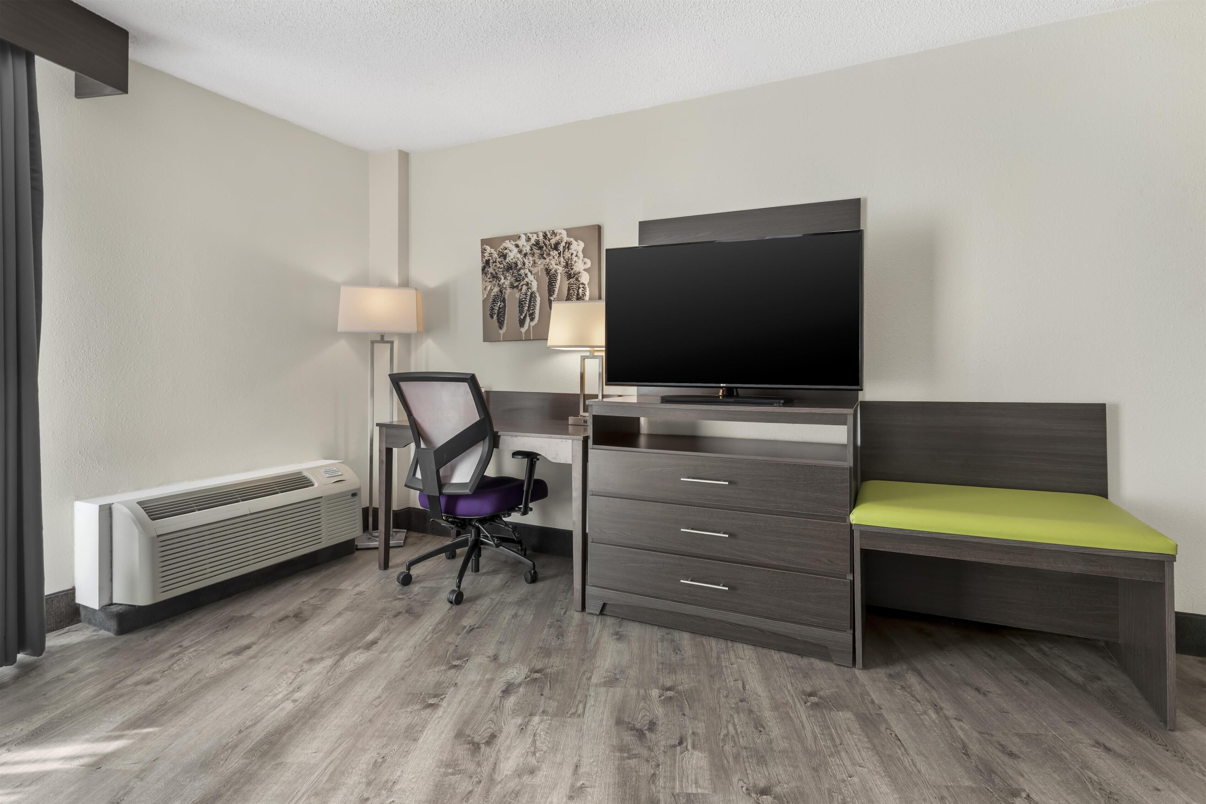 Habitación de hotel con cama, escritorio, silla, televisor de pantalla plana, lámpara y radiador.