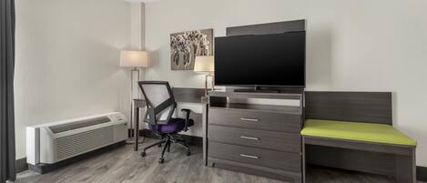 A hotel room with a bed, a desk with a chair, a flat-screen TV, a lamp, and a radiator.