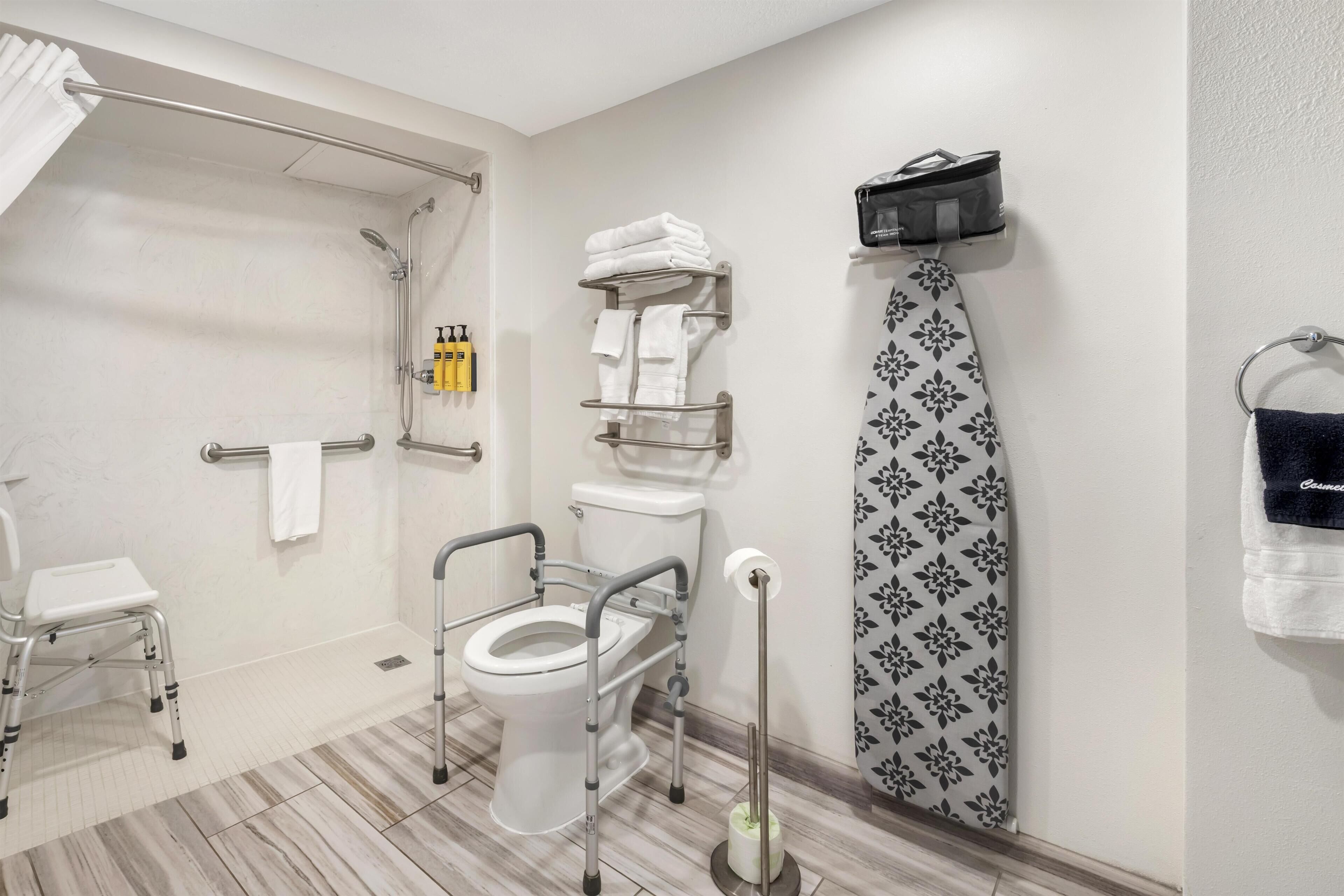 A bathroom with a toilet, a shower, a towel rack, a step stool, and a wall-mounted ironing board.