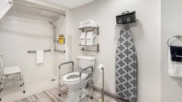 A bathroom with a toilet, a shower, a towel rack, a step stool, and a wall-mounted ironing board.