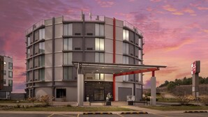 Un hôtel à plusieurs étages, doté d’une entrée couverte, d’une bande verticale rouge qui attire l’attention et d’une enseigne indiquant la présence d’un centre de remise en forme.