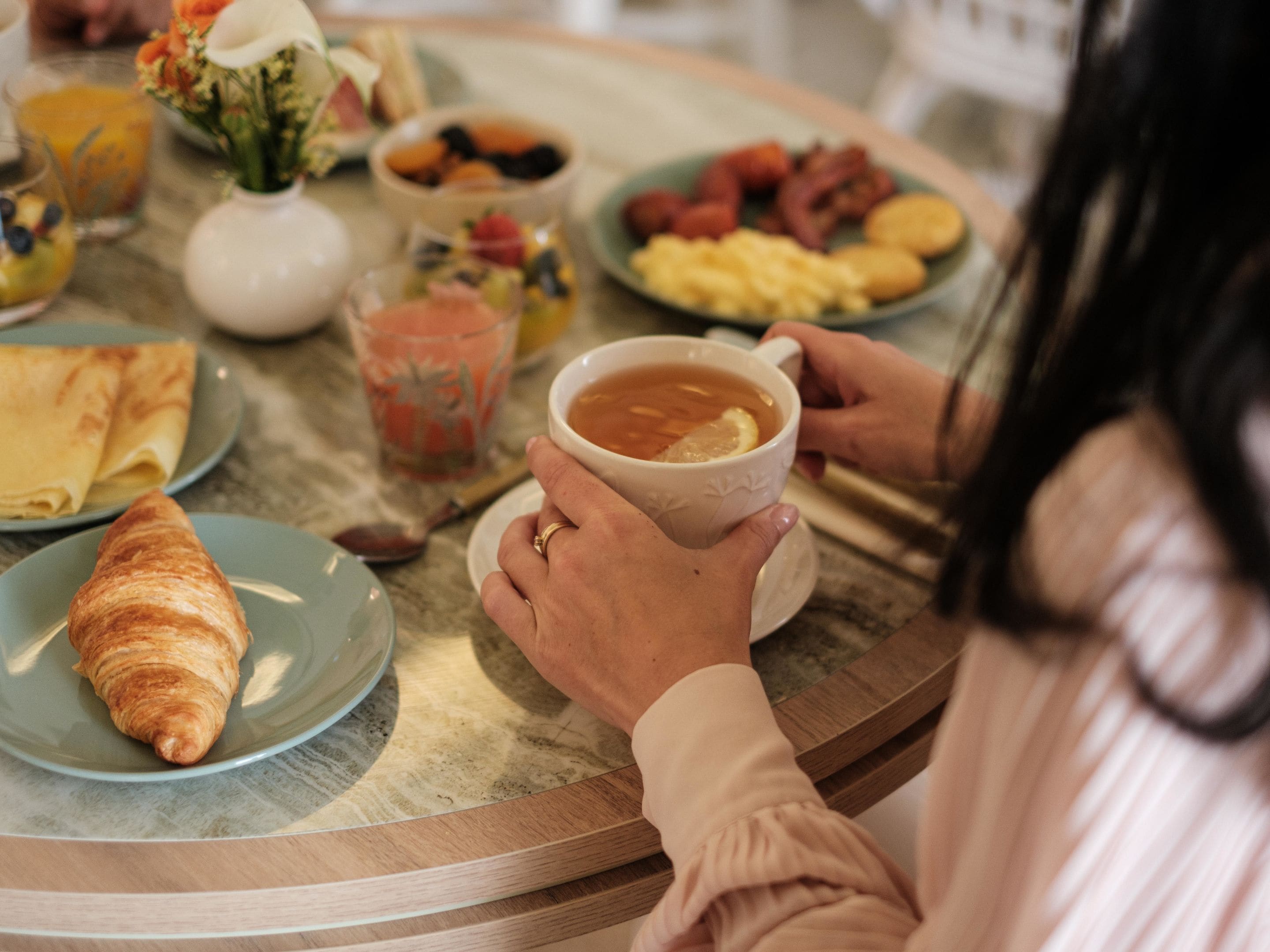 Une table dressée pour le petit-déjeuner, avec un croissant, une tasse de thé, ainsi que divers fruits et pâtisseries.