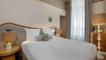 Quarto de hotel com uma cama grande, duas mesas de cabeceira com luminárias, um relógio na parede e uma janela com cortinas.