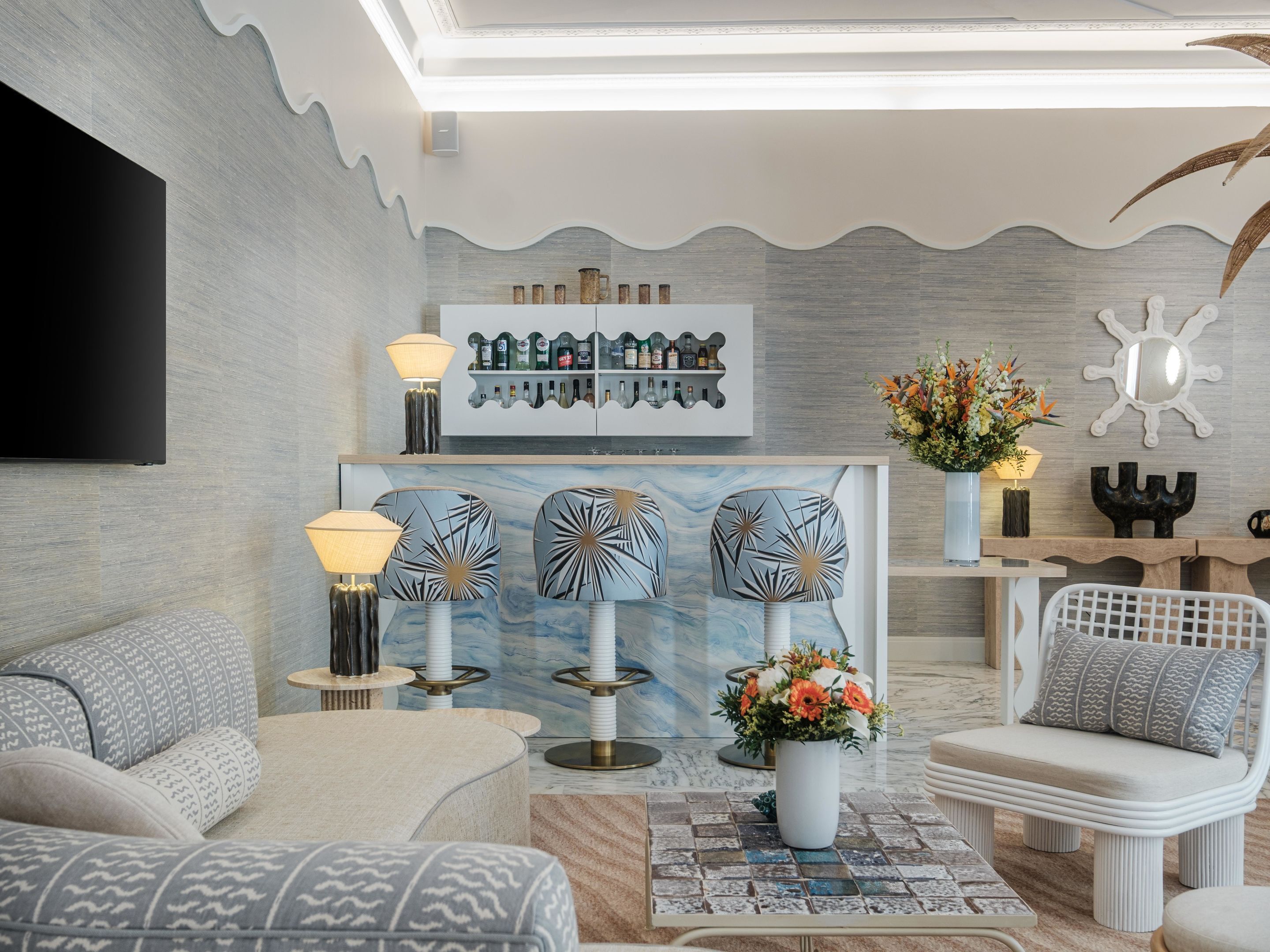 A modern living room with a flat-screen TV, patterned sofas, a coffee table, and a decorative wall unit with bottles.