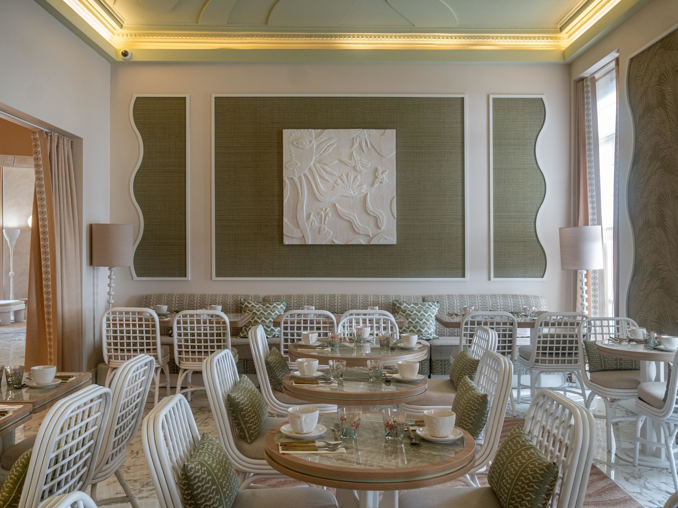 Un comedor con mesas redondas, sillas blancas y cojines estampados verdes.