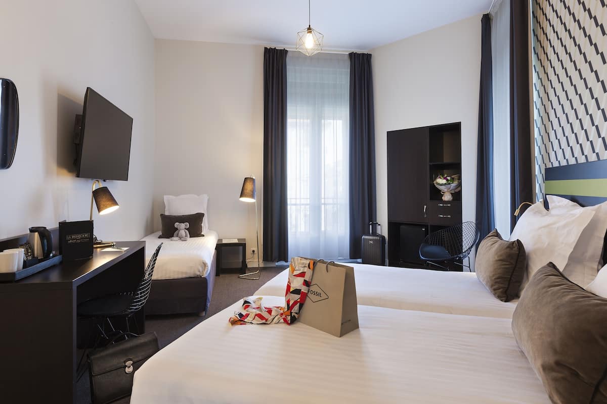 A hotel room with a bed, desk, chair, TV, and a window with curtains.