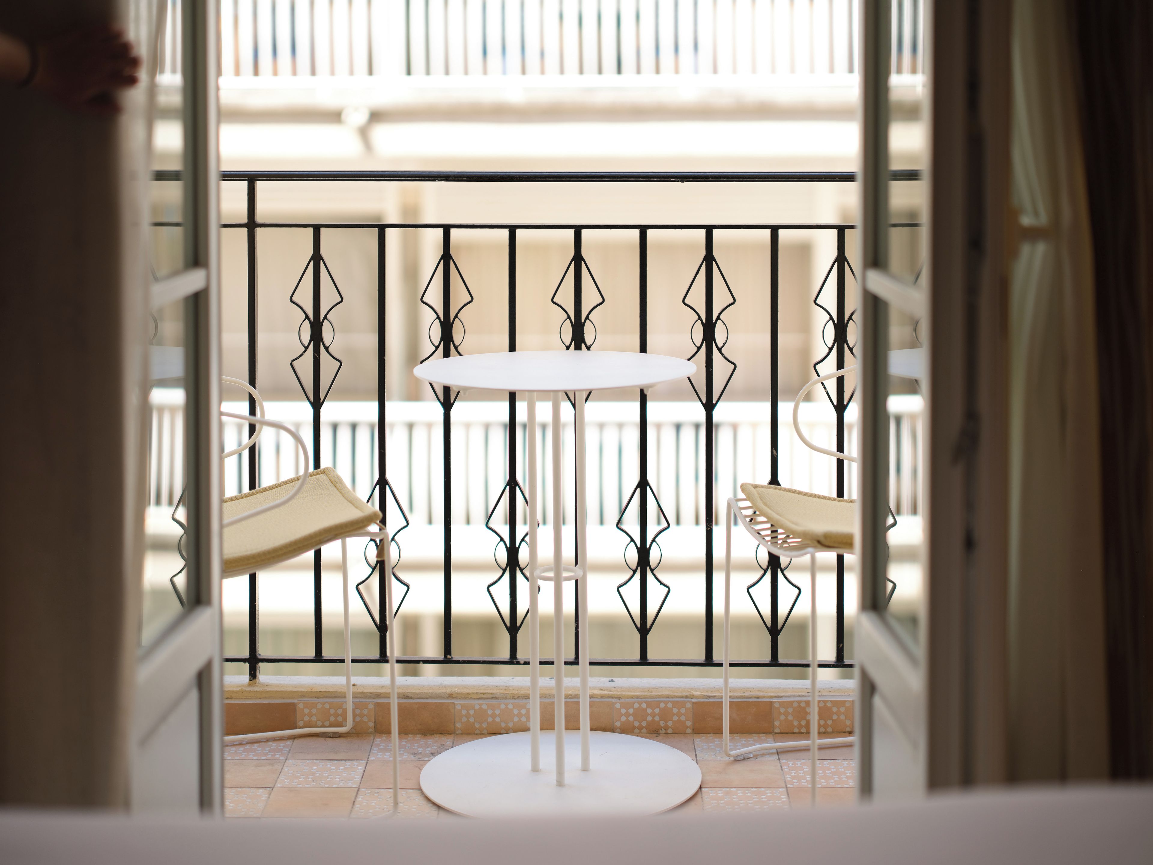 A balcony with a white table and two chairs, a metal railing, and a view of the street.