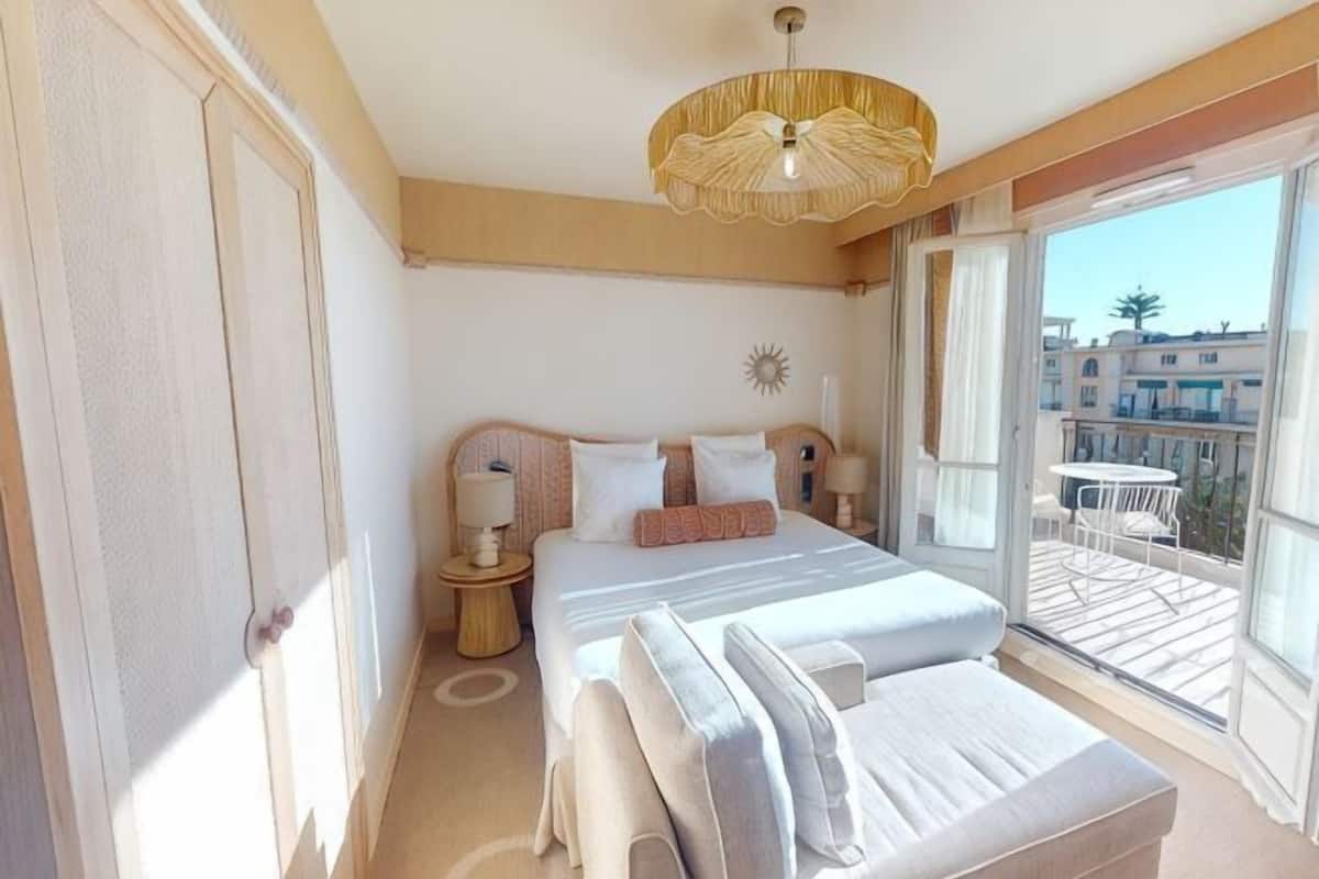 A bedroom with a large bed, a bedside table, a lamp, and a view of the outside balcony.
