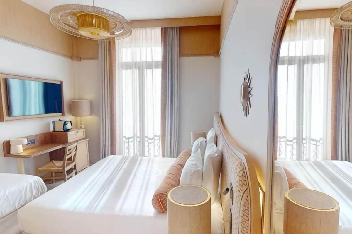 A hotel room with a large bed, a desk, a television, and a balcony view.