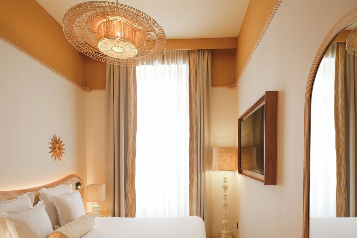 A hotel room with a large bed, a round chandelier, a mirror, and a sun decoration on the wall.
