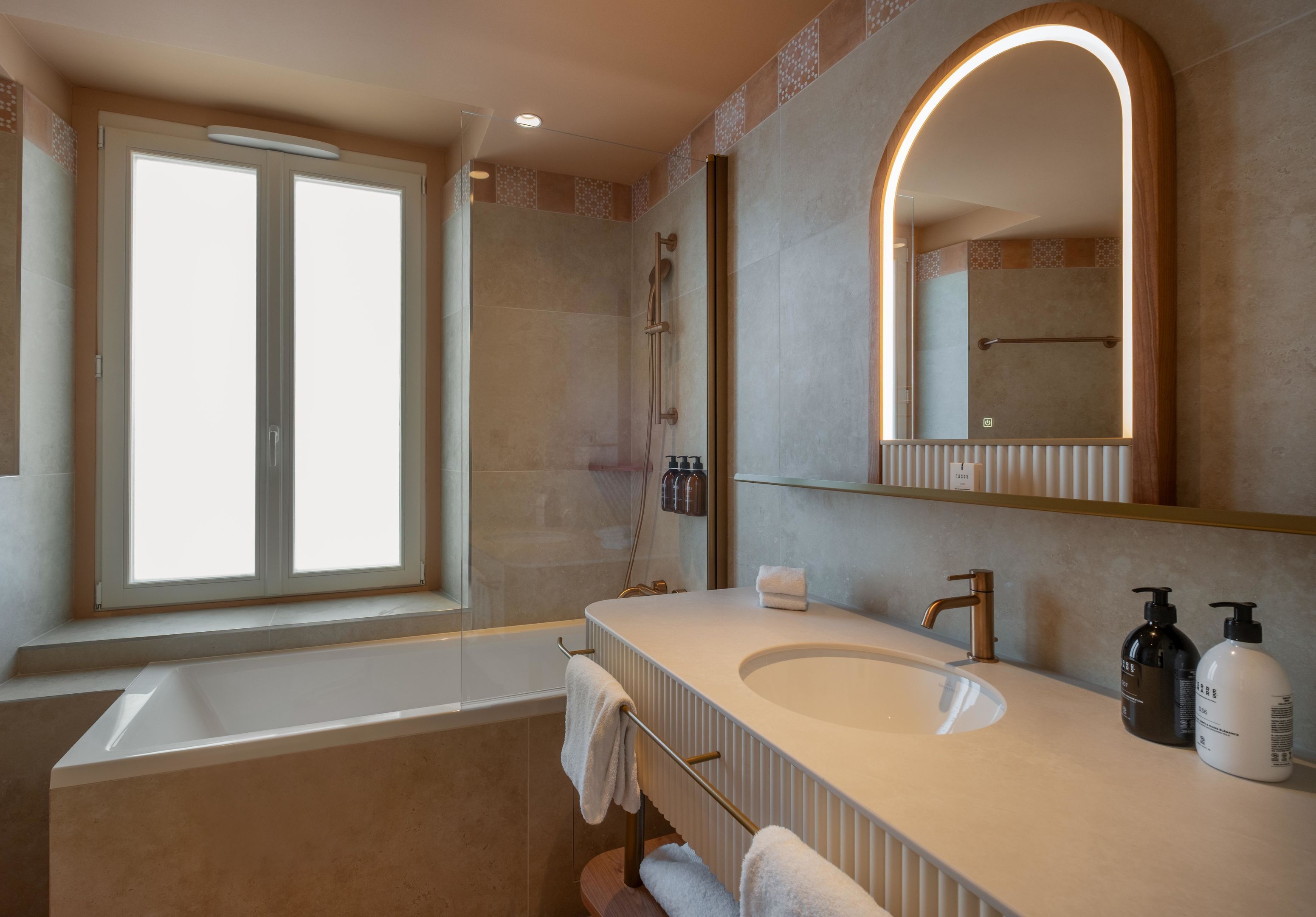 A modern bathroom with a bathtub, a large mirror, and a vanity with a sink and two bottles of soap.