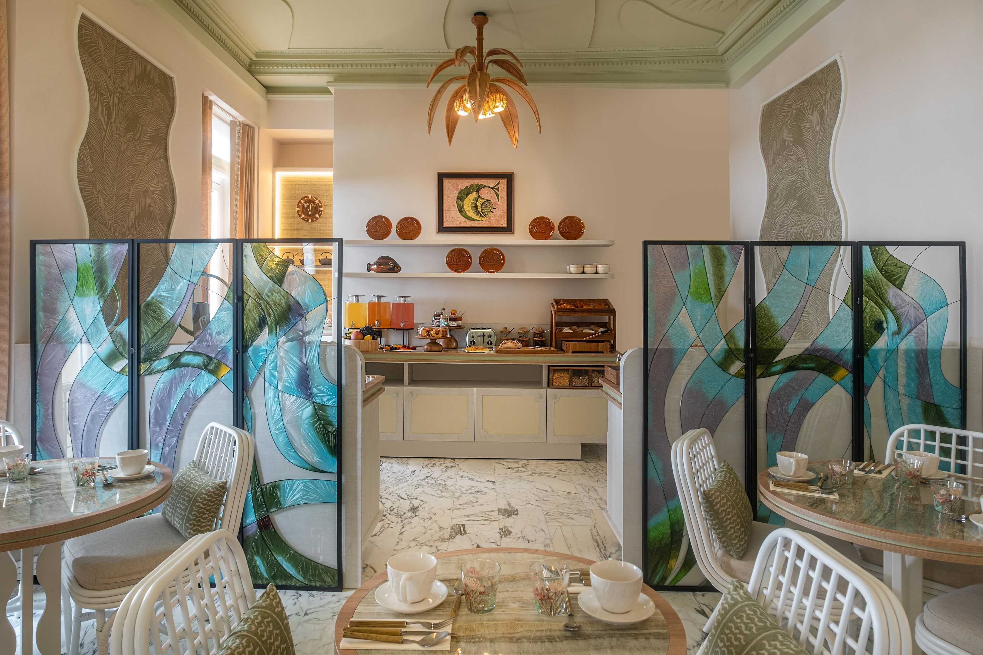 Un comedor con un separador de vidrio, sillas blancas, piso de mármol y una cocina al fondo.