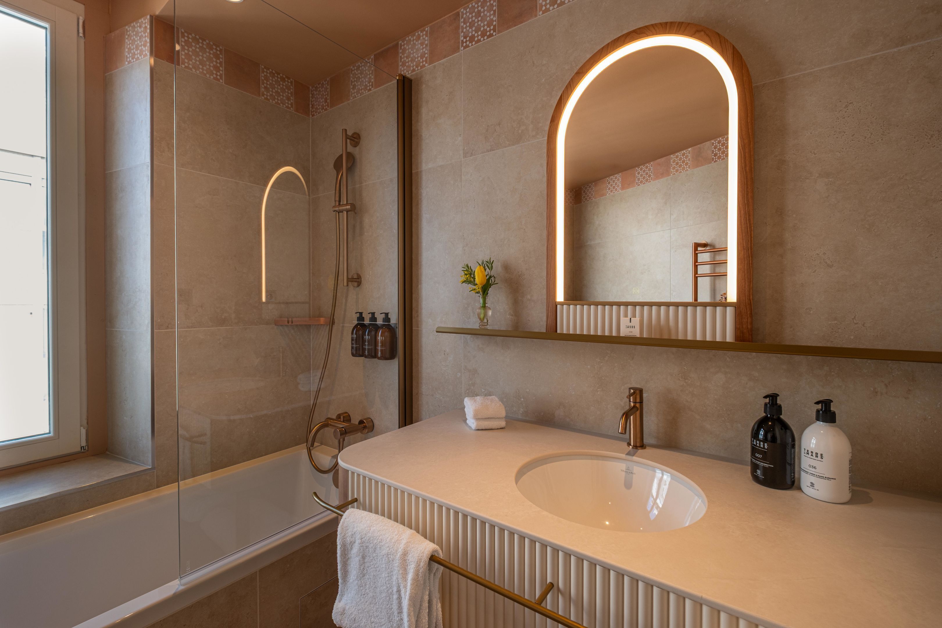 Ein modernes Badezimmer mit einem großen Spiegel, einer Badewanne und einem Waschtisch mit Spüle und Handtuchhalter.