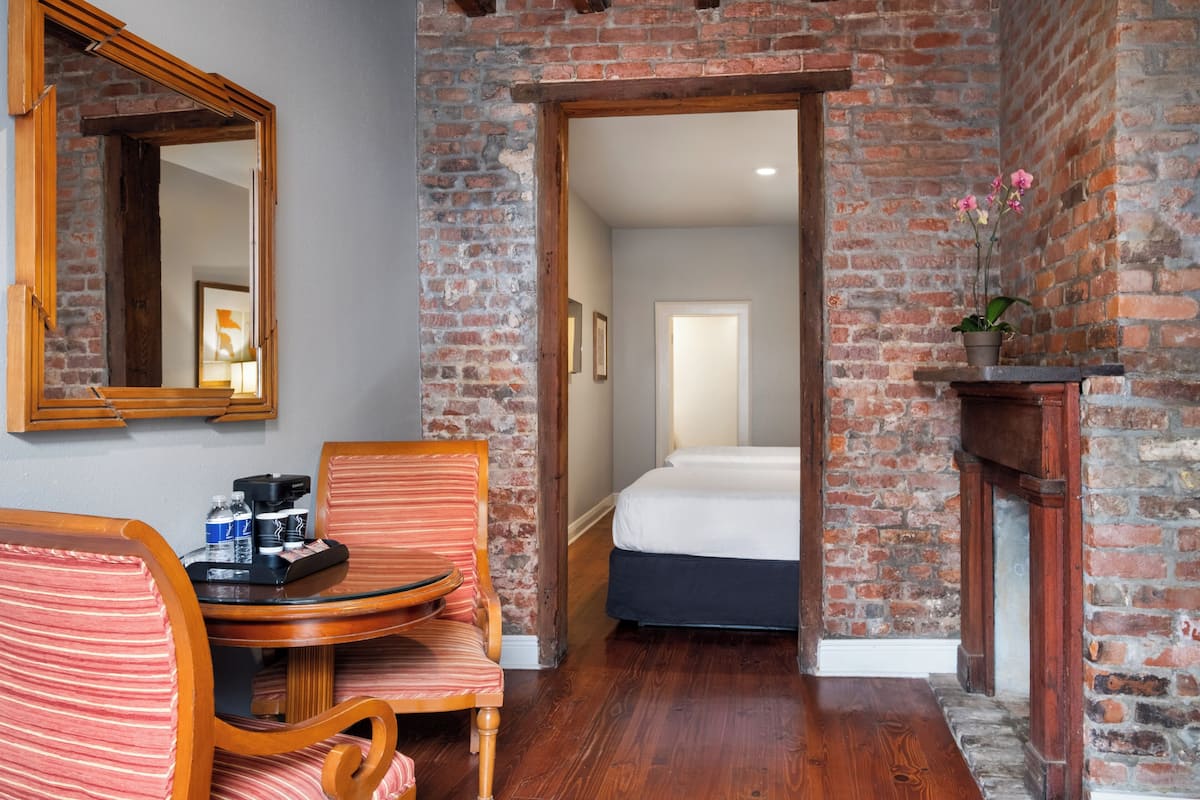 A hotel room with a brick wall, a wooden chair, a small table with a tray, a bed, and a mirror.