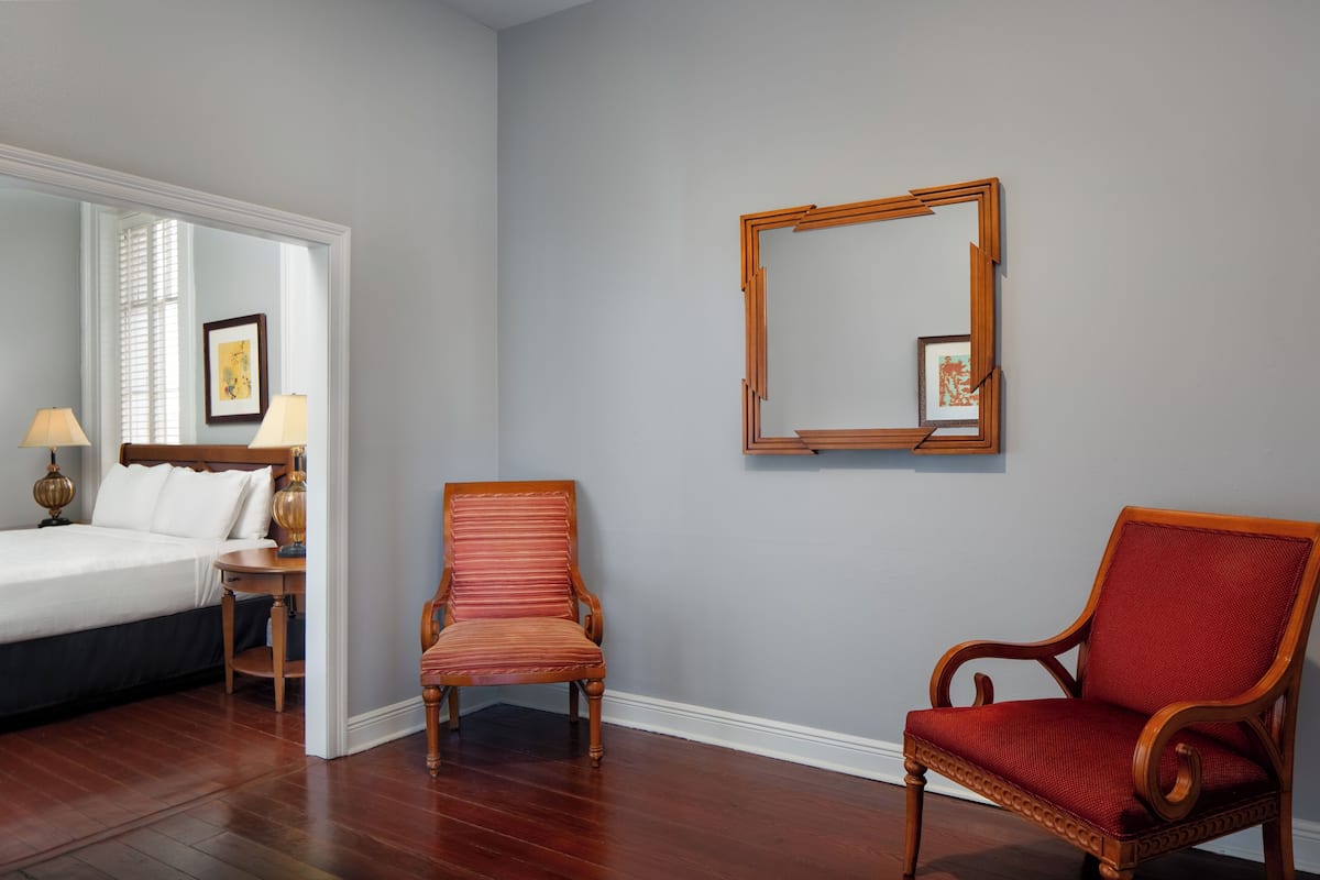 A hotel room with a bed, two chairs, a nightstand, a lamp, and a framed picture on the wall.