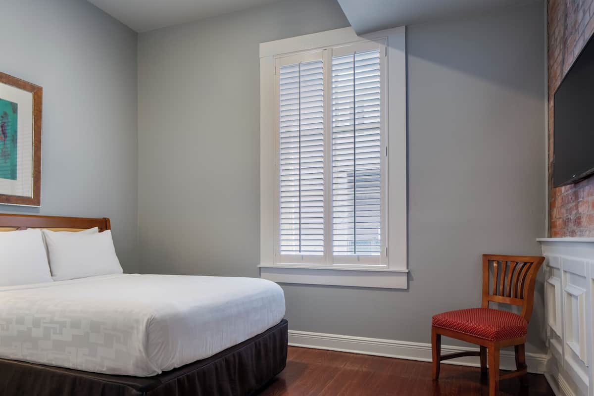 A bedroom with a bed, a window with blinds, a chair, and a fireplace.
