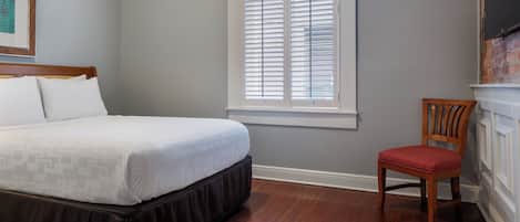 A bedroom with a bed, a window with blinds, a chair, and a fireplace.