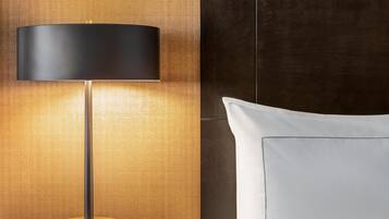 A modern lamp with a cylindrical shade, a wooden textured wall, and a white pillow on a bed.