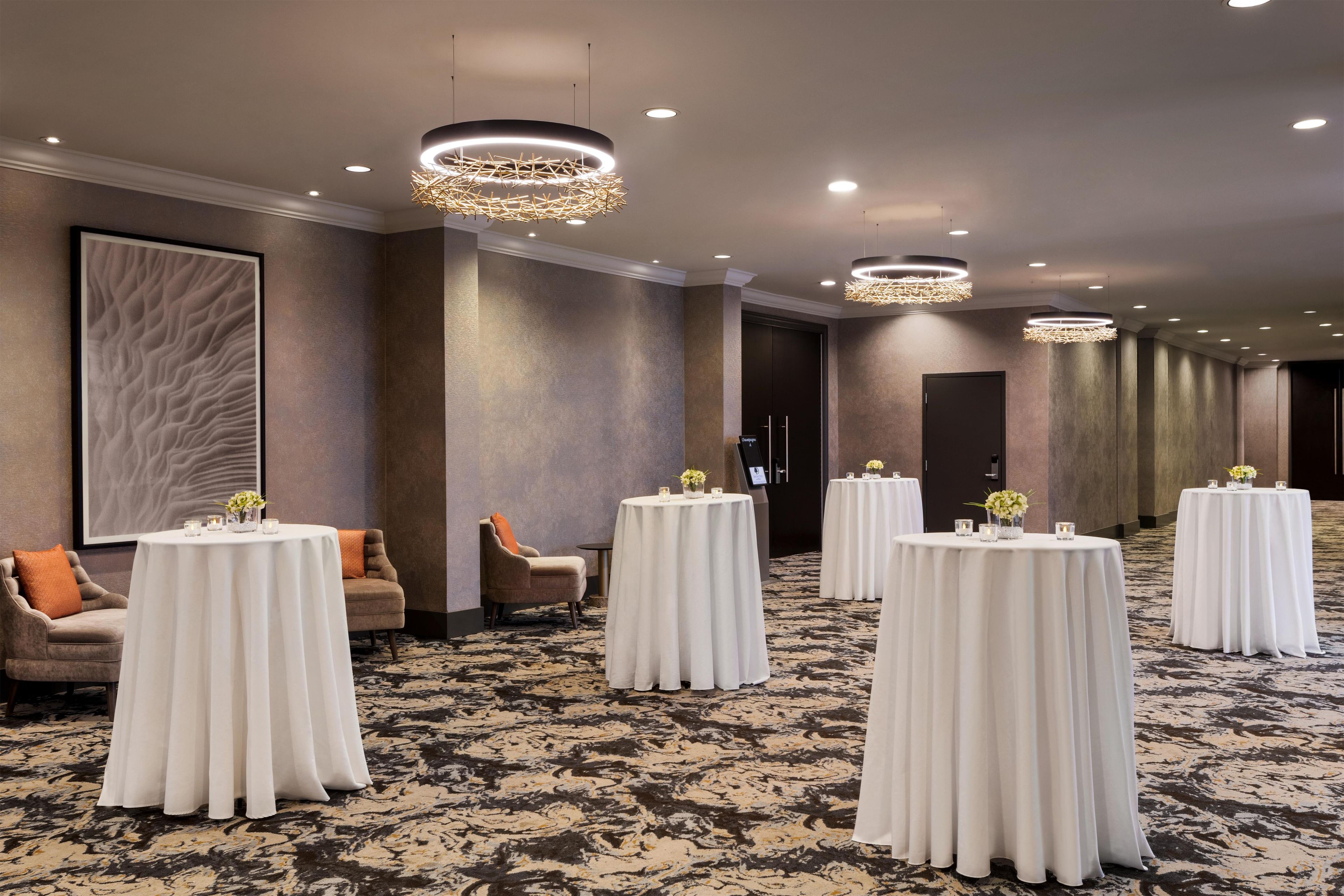 A hotel corridor with round tables, chairs, and a carpeted floor.