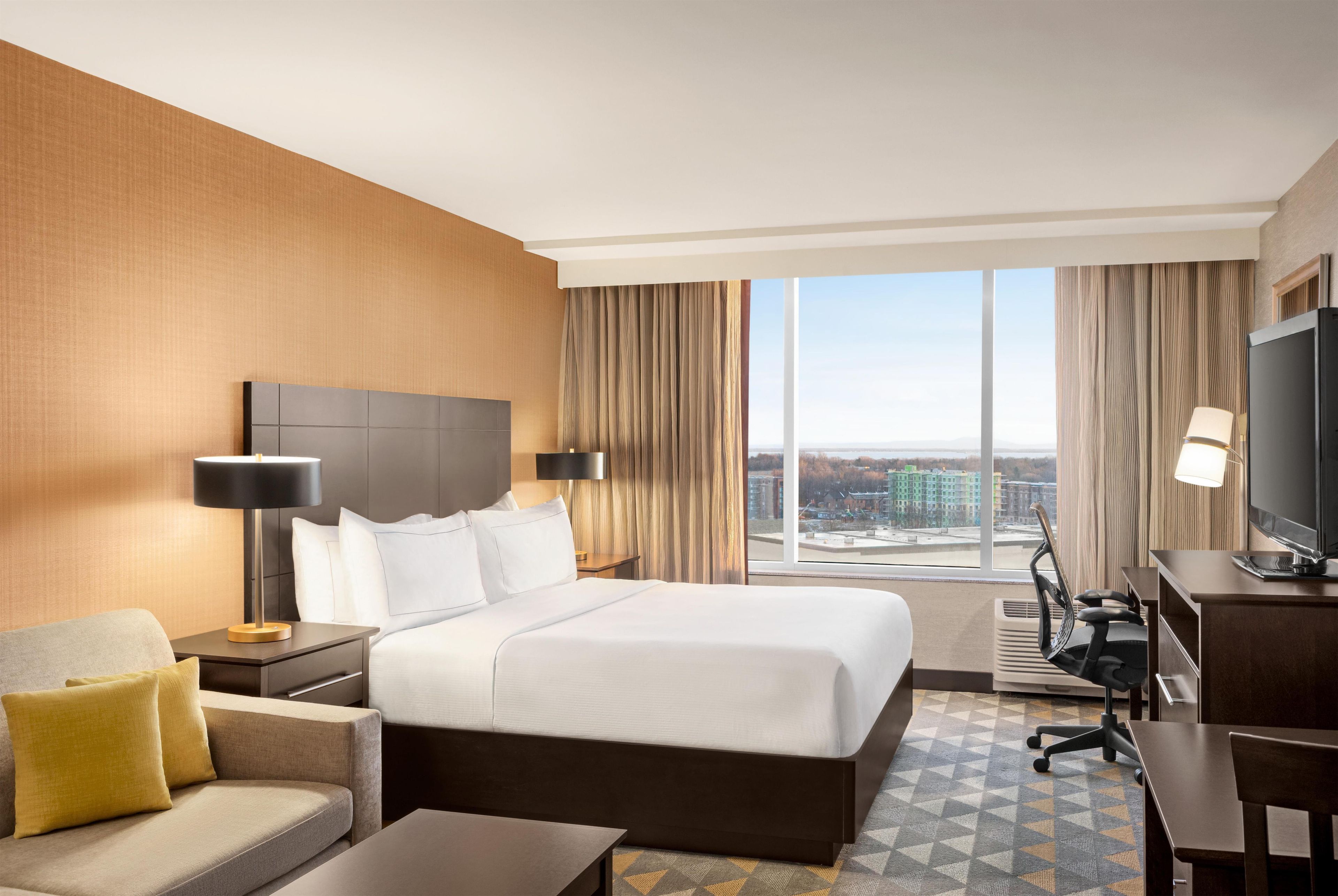 A hotel room with a bed, a desk, a chair, a sofa, and a TV.