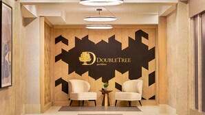 A reception area with two sofas, a wall-mounted logo, and a modern light fixture. - DoubleTree by Hilton Pointe Claire Montreal Airport West (Pointe Claire)