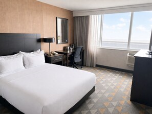 Een hotelkamer met een groot bed, een bureau, een stoel, een spiegel en een raam met gordijnen.