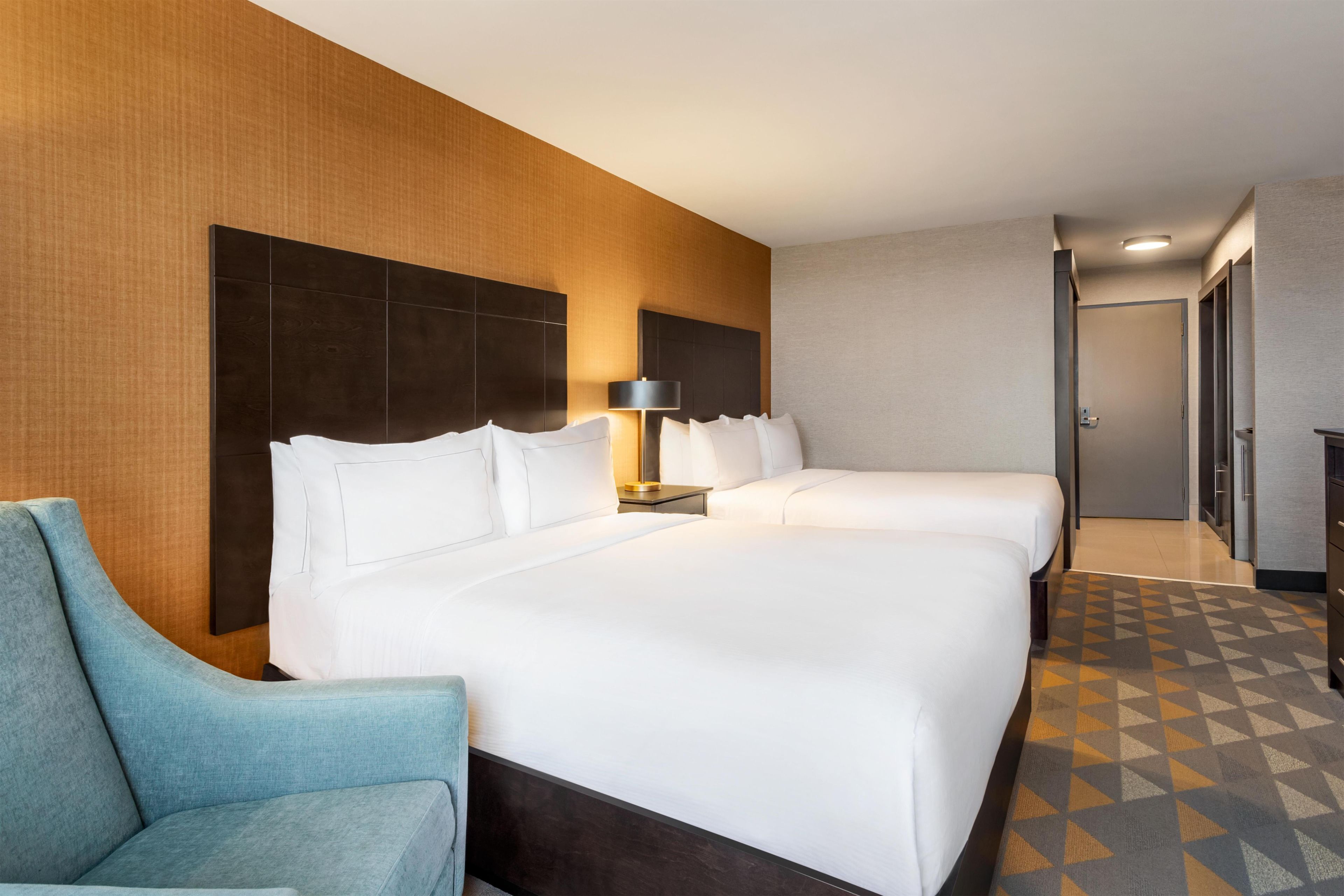 A hotel room with a large bed, two bedside tables, a lamp, a chair, and a geometric patterned floor.