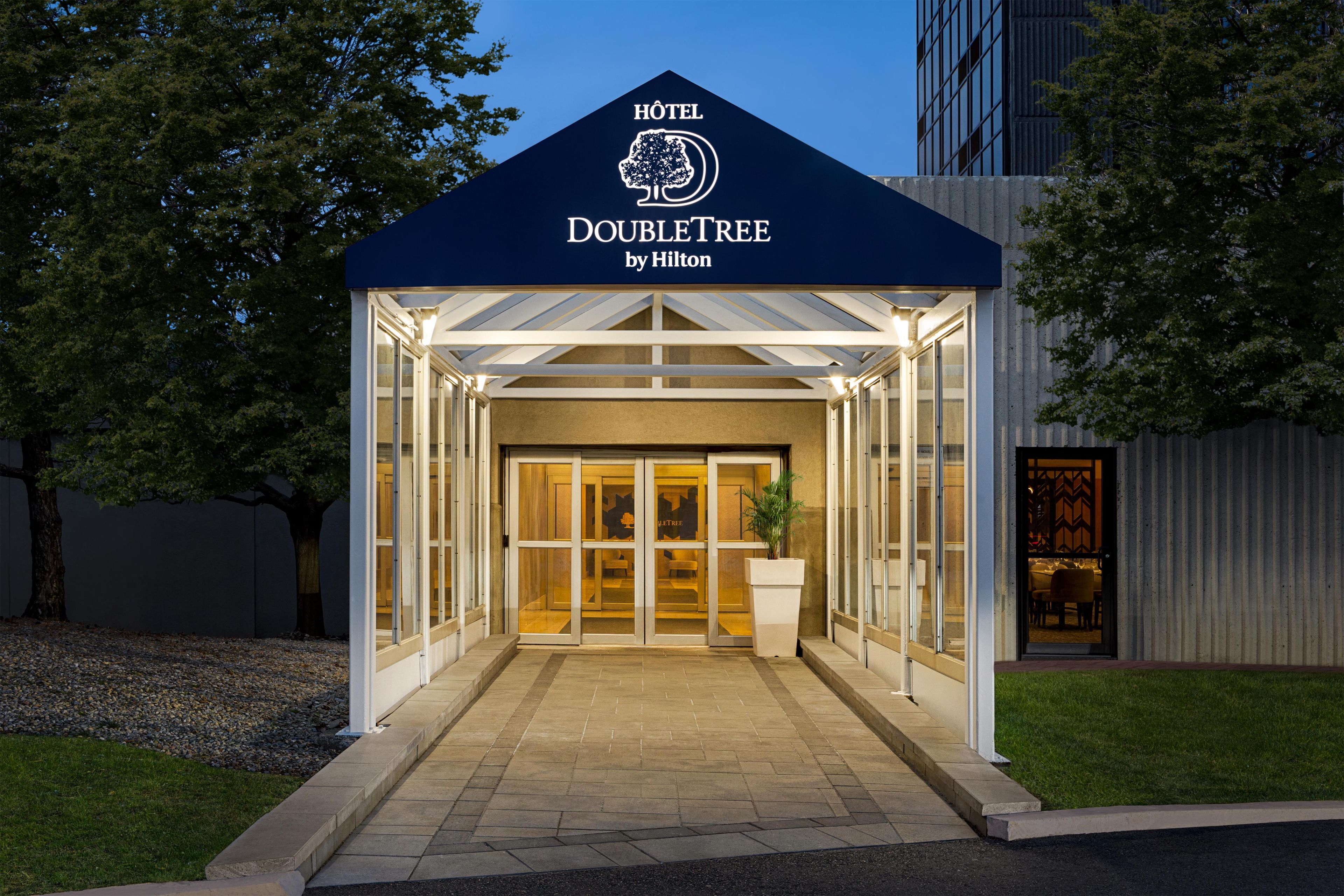A hotel entrance with a glass facade, a sign above reading 'HOTEL DOUBLETREE by Hilton,' and a well-lit pathway leading to the entrance.