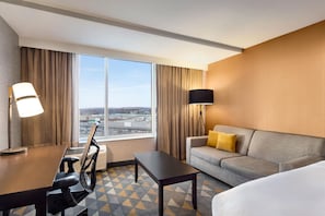 Une chambre d’hôtel équipée d’un bureau, d’une chaise, d’un canapé et d’une grande fenêtre donnant sur la ville.