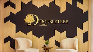 A room with two beige armchairs, a small round table with a plant, and a wall with a geometric pattern and the logo 'DOUBLETREE par Hilton'.