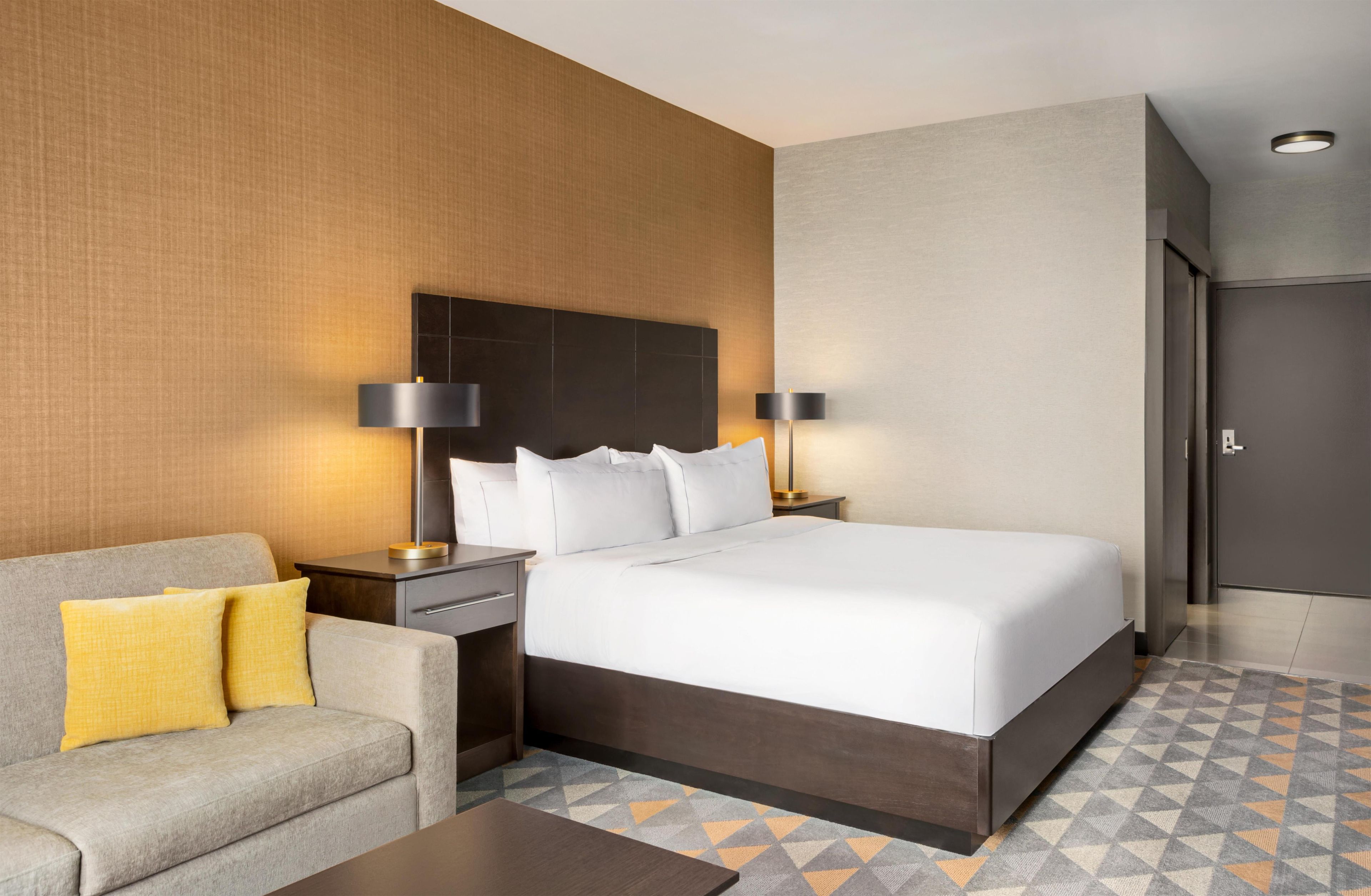 A hotel room with a bed, nightstands, a sofa, and a patterned floor.