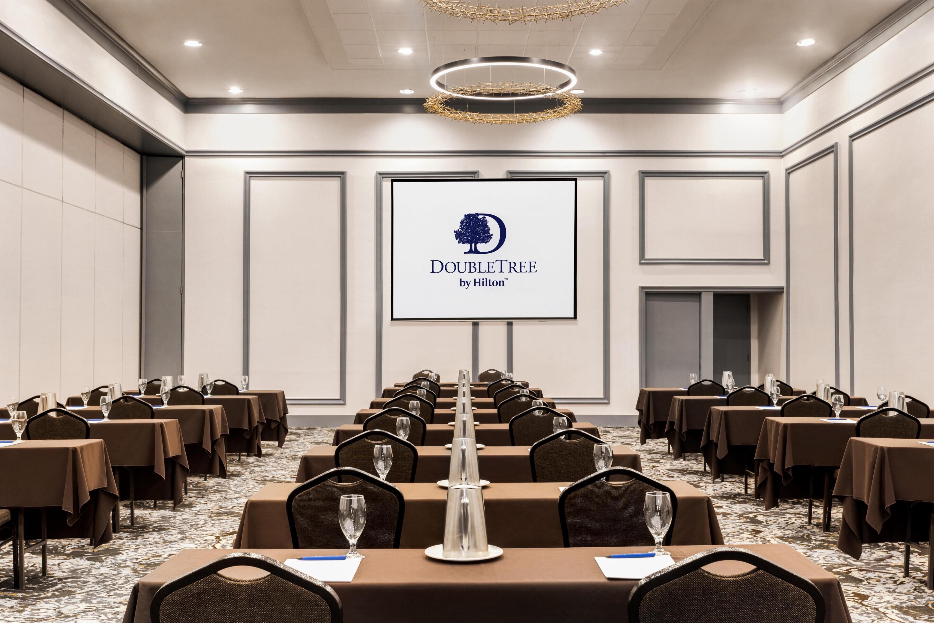 A conference room with tables, chairs, and a podium with a logo.