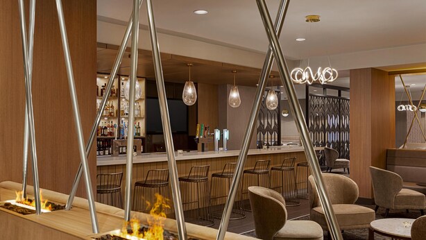 A bar area with a fire feature, seating, and a bar counter with bottles. - DoubleTree by Hilton Pointe Claire Montreal Airport West (Pointe Claire)