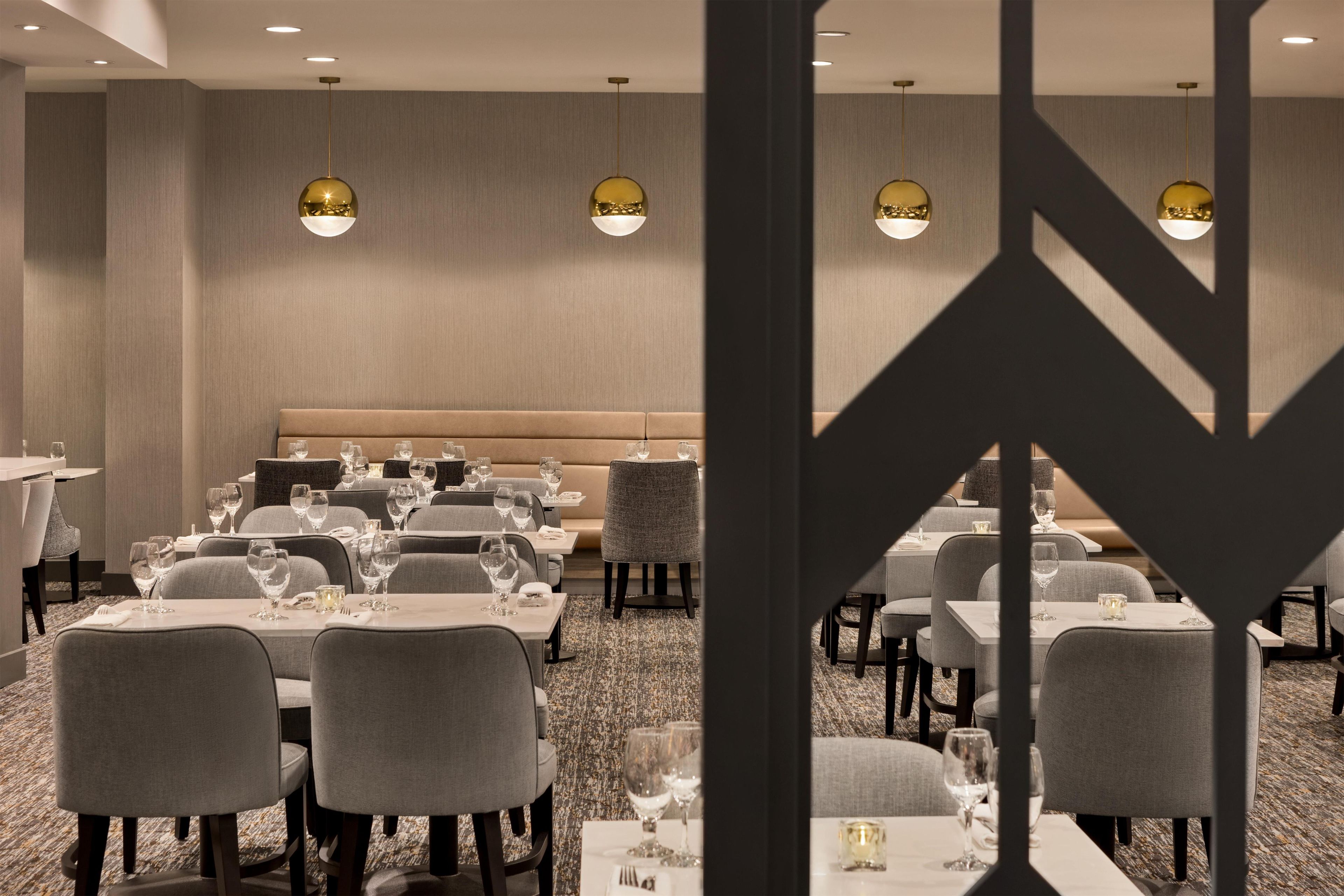 A hotel dining area with tables, chairs, and pendant lighting.