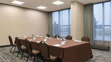 Un salón de conferencias con una larga mesa, sillas y vistas a un paisaje urbano a través de amplios ventanales.