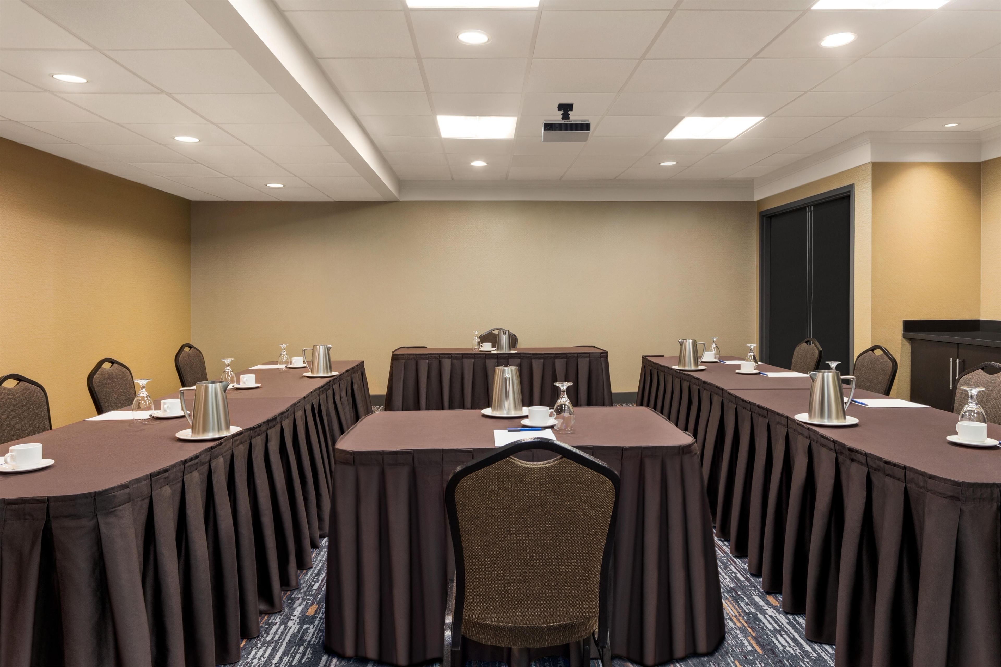 A conference room with a long table, chairs, and a projector on the ceiling.